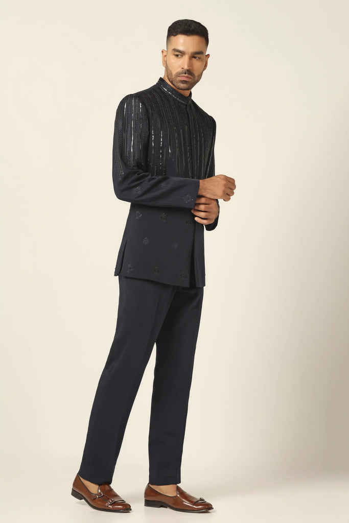 Elevate your style with our Navy bandhgala, crafted in all-weather suiting fabric. Featuring contemporary design with thread embroidery and metal tape, paired with black trousers.
