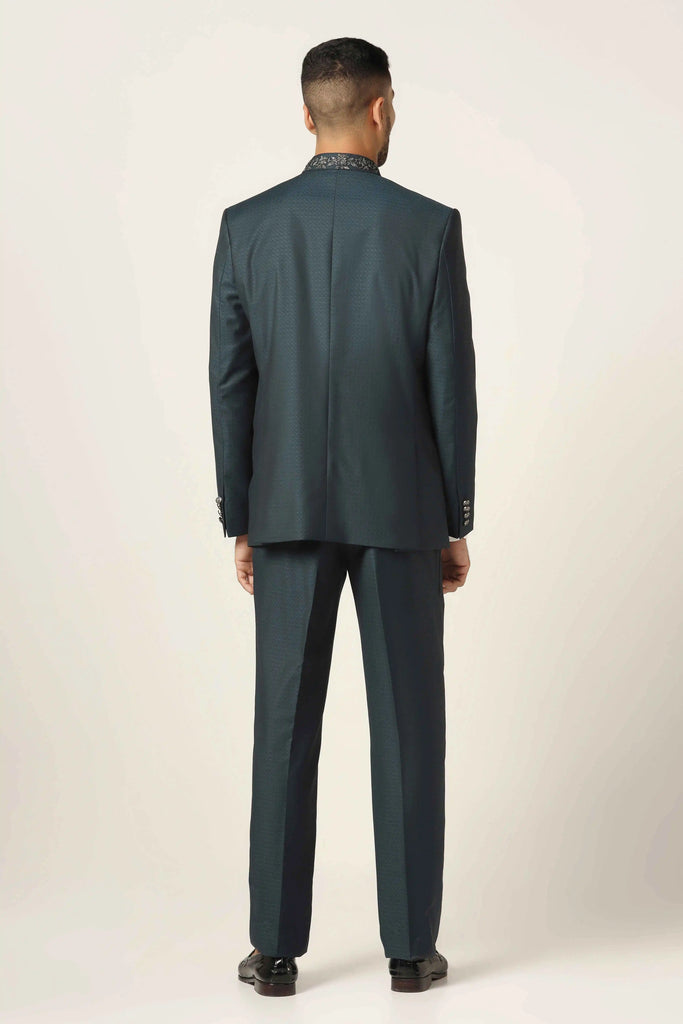 Step into refined style with our green textured Bandhgala suit, crafted from all-weather wool blend fabric. Enhanced with metallic silver buttons and collar embroidery.