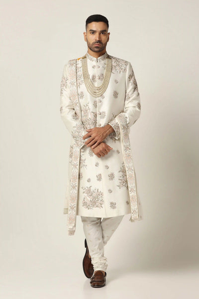 Experience timeless elegance with our classic Sherwani, adorned with bold Zari embroidery in a floral pattern. Silver accents enhance its sophistication.