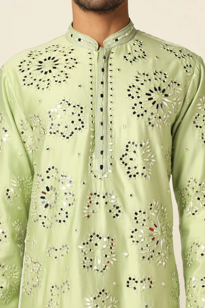 This Kurta Pajama set is crafted from luxurious Chanderi silk fabric. The green Kurta features exquisite mirror embroidery and threadwork, paired with off-white churidar pajamas for a sophisticated look.