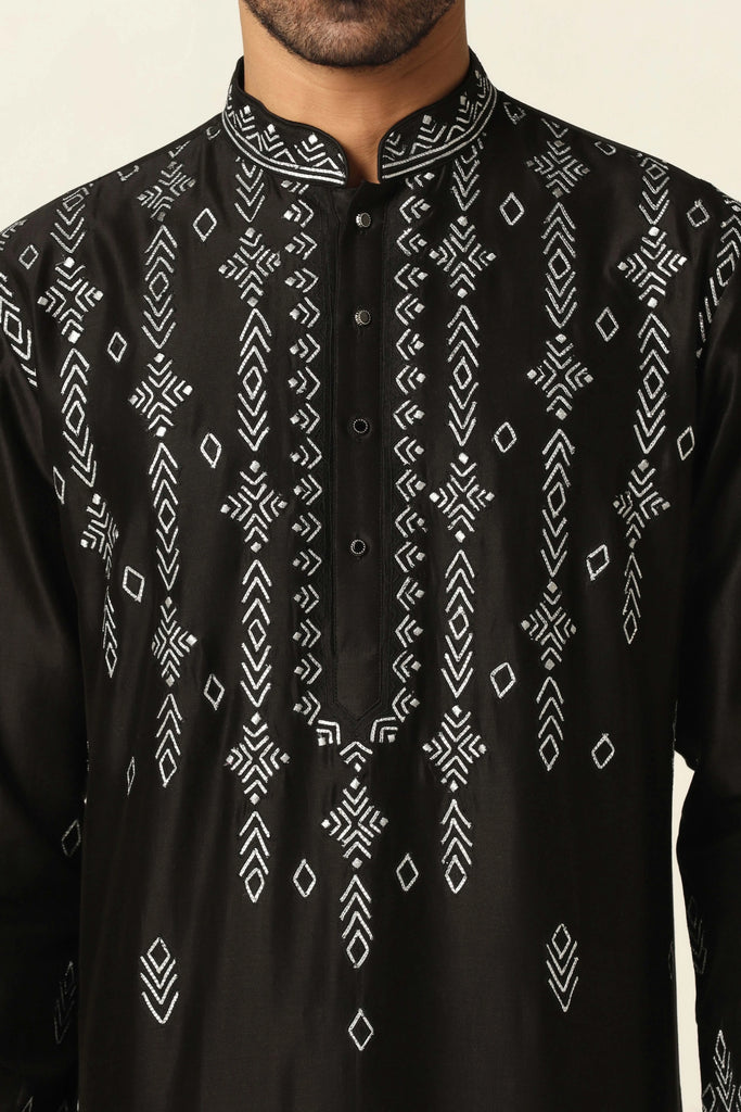 Elevate your ethnic look with this Chanderi silk kurta pajama set. The black kurta features striking hand embroidery, paired with off-white churidar pajamas for a timeless appeal.