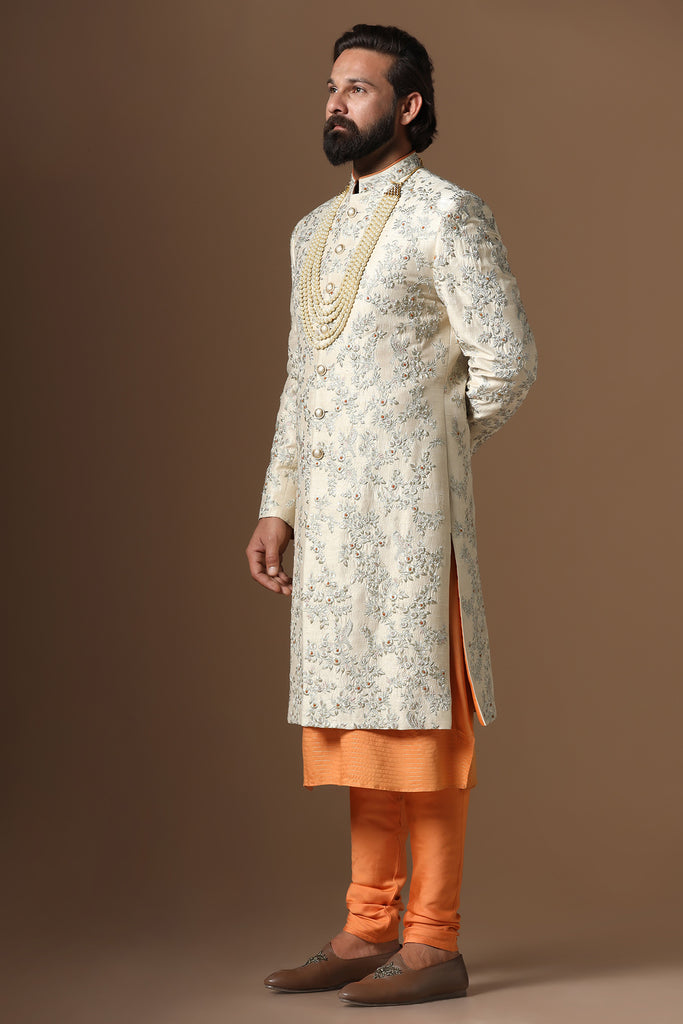 Embrace sophistication with our beige floral embroidered Sherwani paired with an orange kurta and pajama. Accessories sold separately.