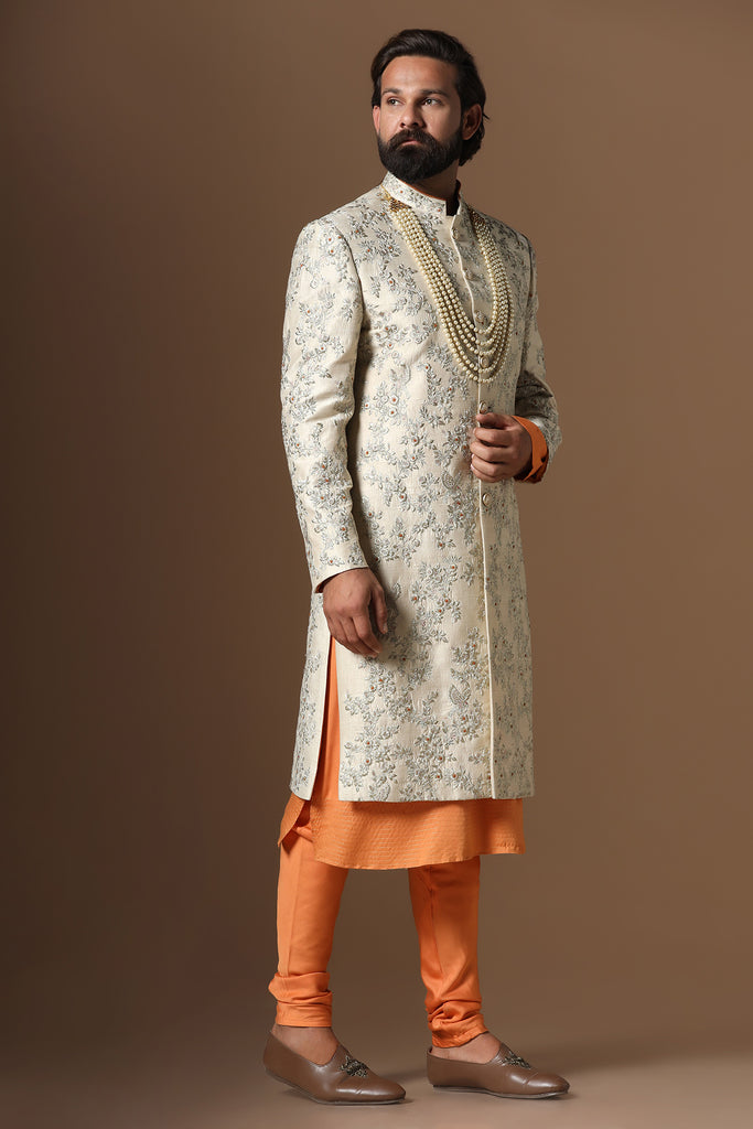 Embrace sophistication with our beige floral embroidered Sherwani paired with an orange kurta and pajama. Accessories sold separately.