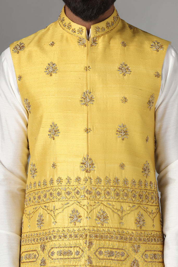 Radiate charm in our yellow raw-silk Nehru jacket with geometric and floral embroidery. Paired flawlessly with a coordinated off-white kurta pajama set.