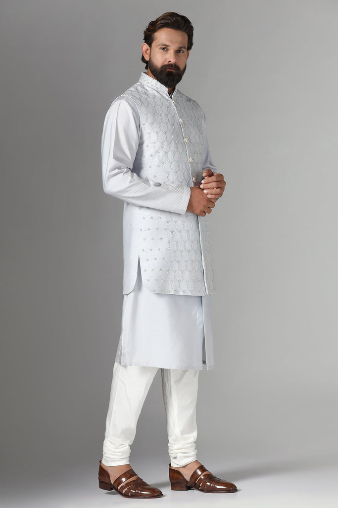 Elevate your style with our long grey raw silk Nehru Jacket, adorned with geometric embroidery. Paired seamlessly with a monochrome kurta pajama ensemble.