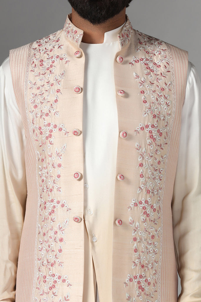 Elevate your style with our light peach raw silk Nehru Jacket adorned with floral embroidery and pintucks. Paired with an ombre pleated kurta and pajama for a stunning ensemble.