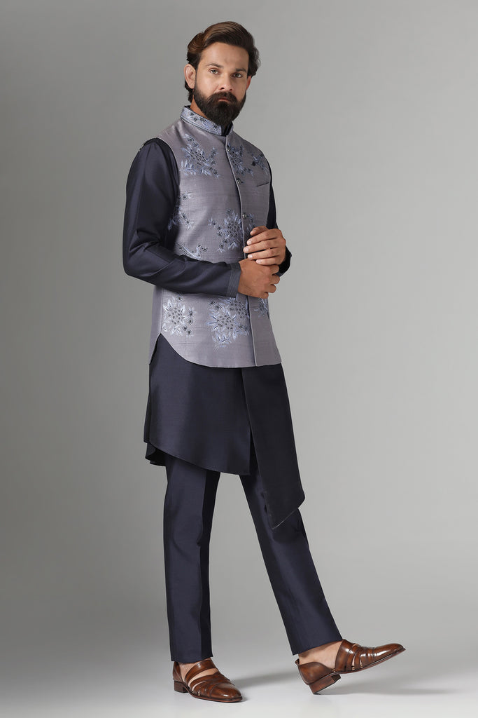 Enhance your style with our grey raw silk Nehru jacket adorned with floral embroidery. Paired with a black asymmetric kurta pajama for a striking ensemble.