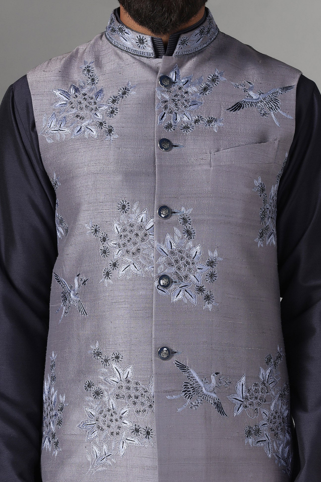 Enhance your style with our grey raw silk Nehru jacket adorned with floral embroidery. Shop Now!