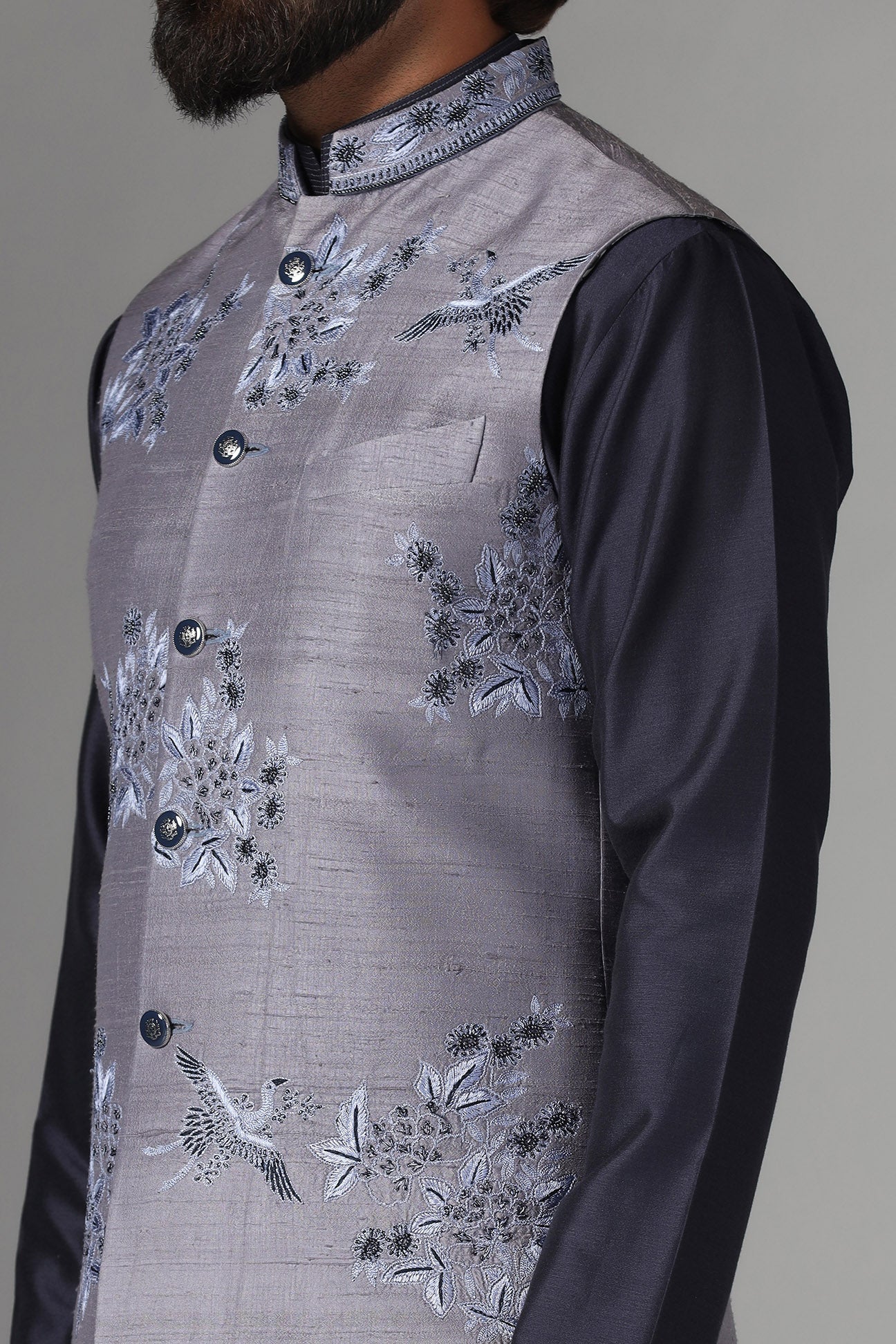 Enhance your style with our grey raw silk Nehru jacket adorned with floral embroidery. Shop Now!