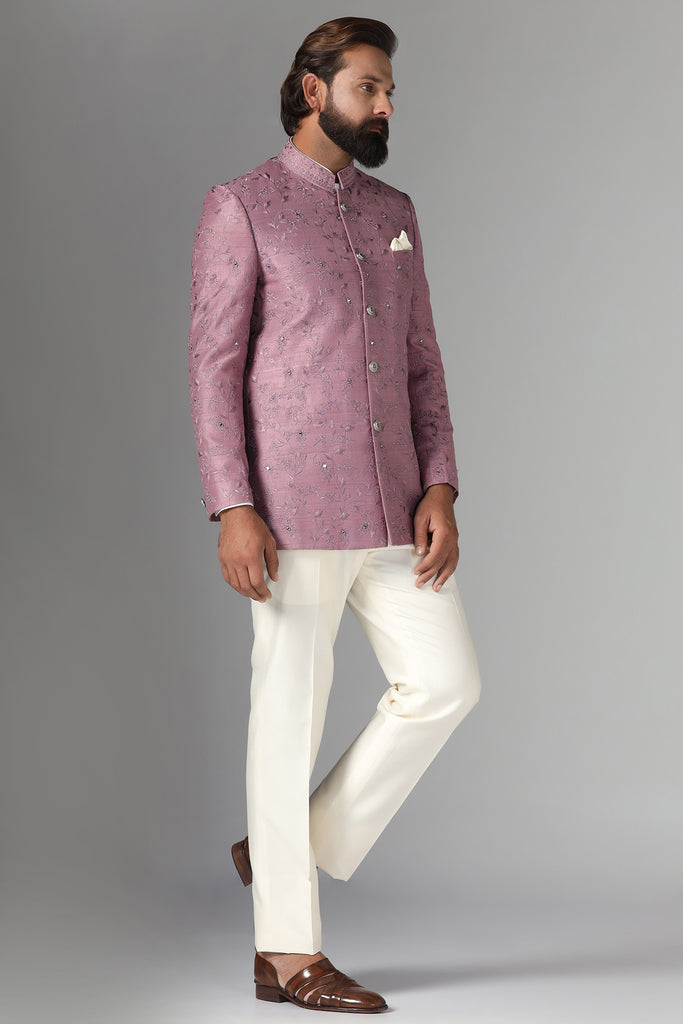 Elevate your style with our onion-pink Bandhgala suit in raw-silk fabric, adorned with floral embroidery. Paired with off-white trousers for a refined ensemble.