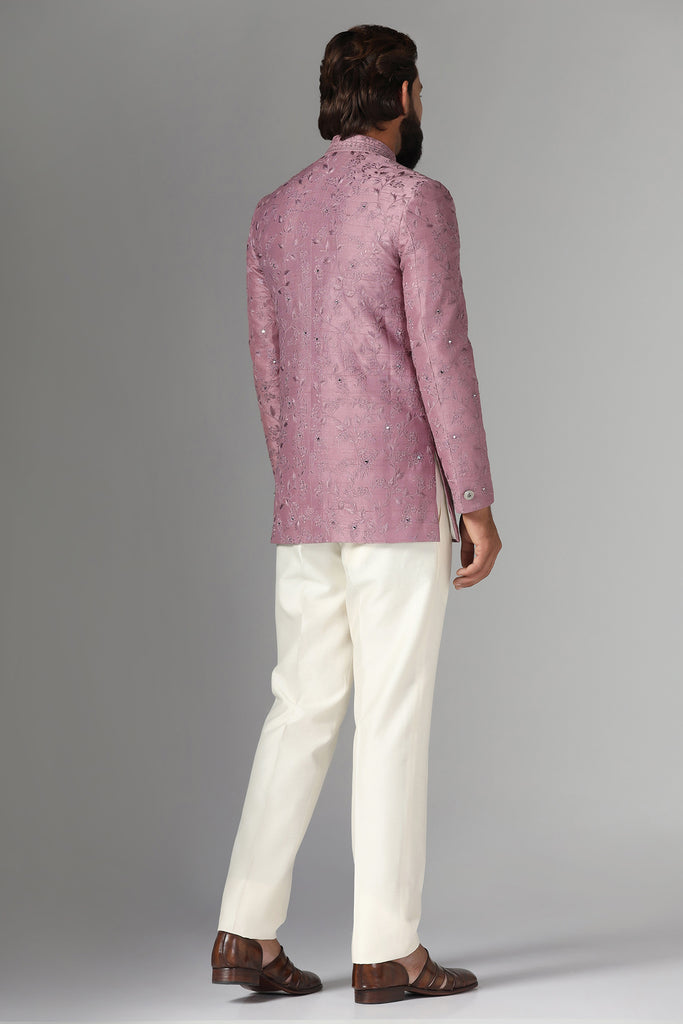 Elevate your style with our onion-pink Bandhgala suit in raw-silk fabric, adorned with floral embroidery. Paired with off-white trousers for a refined ensemble.