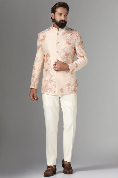 Dress in sophistication with our light peach Bandhgala suit in raw-silk fabric, adorned with floral embroidery. Trousers feature a tapered, flat-front design for timeless elegance.