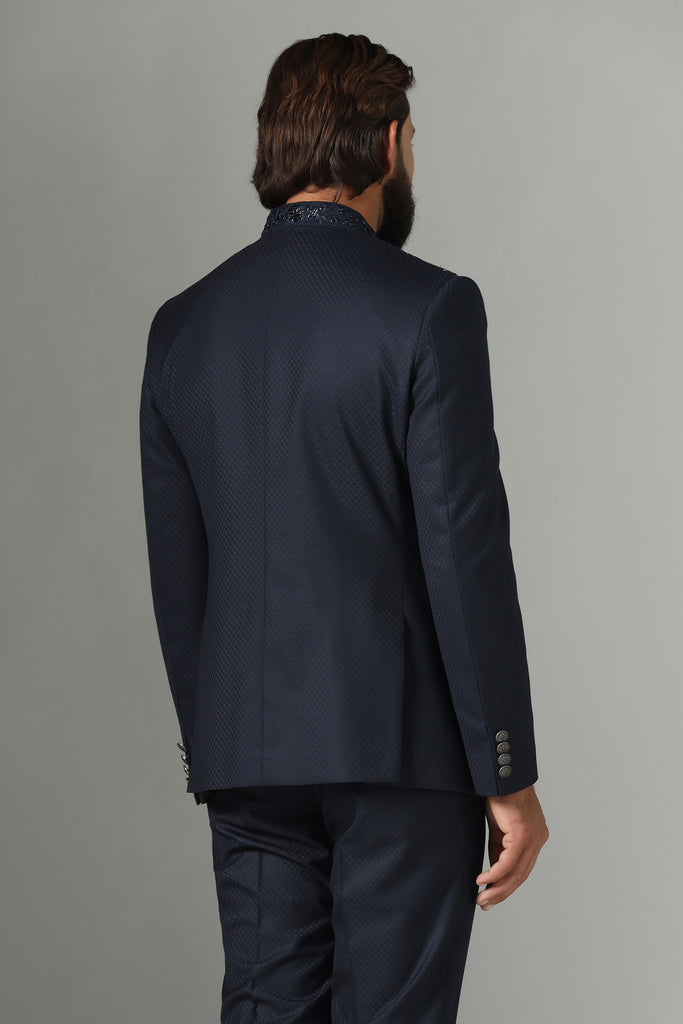 Exude elegance in our midnight blue asymmetric Bandhgala suit, tailored from wool-rich fabric. Highlighted by an embroidered asymmetric panel, paired with tapered, flat-front trousers.