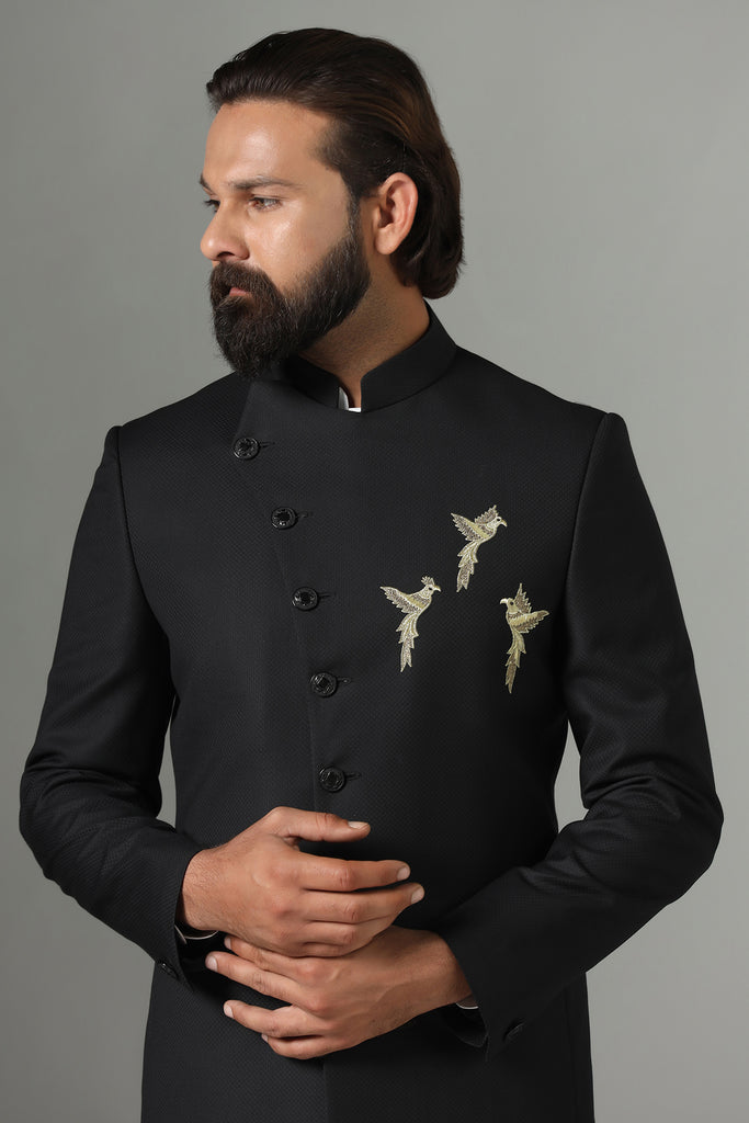 Elevate your occasion with our Asymmetric Black Bandhgala suit. Crafted from luxurious wool-rich fabric, it features intricate bird motif embroidery for a touch of sophistication. Paired with tapered trousers for a sleek finish.