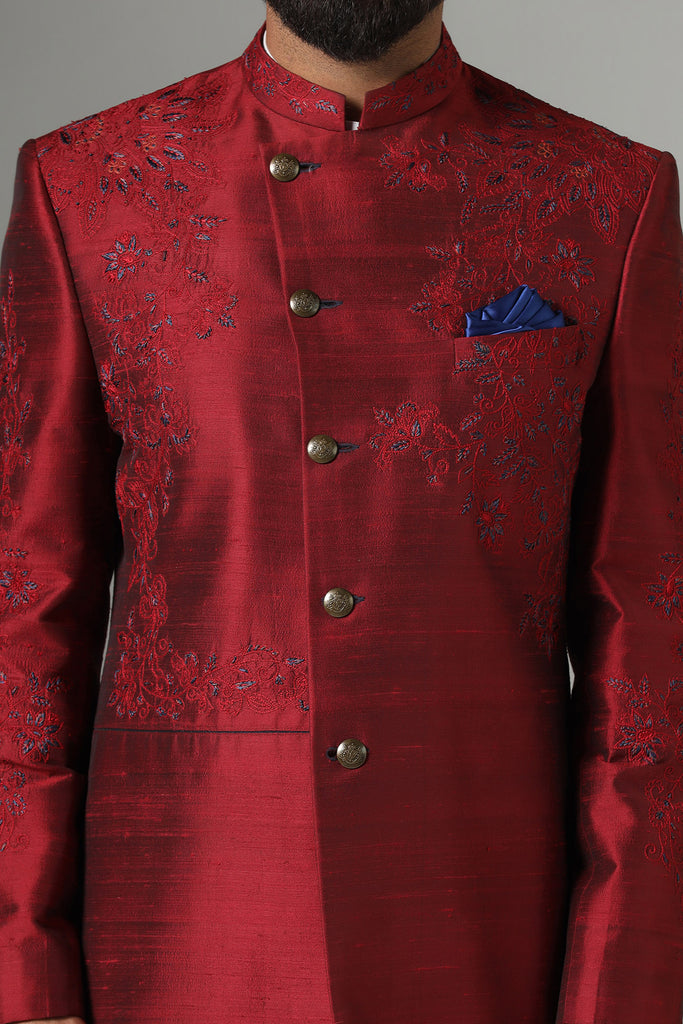 Dress with sophistication in our Red Bandhgala suit, tailored from Raw-Silk fabric and adorned with delicate thread-work embroidery. Paired with navy blue trousers for a refined ensemble.