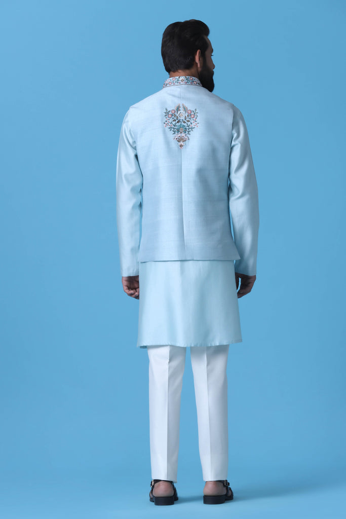 Elevate your style with our Light Blue raw silk Nehru Jacket adorned with floral embroidery and mirror work. Paired with a matching kurta and off-white trousers for timeless elegance.