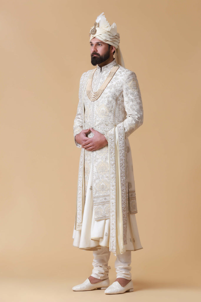 Exude regal elegance in this off-white Sherwani crafted from raw silk, featuring intricate tonal embroidery and patchwork. Paired with a flared kurta and pajama for a complete ensemble.